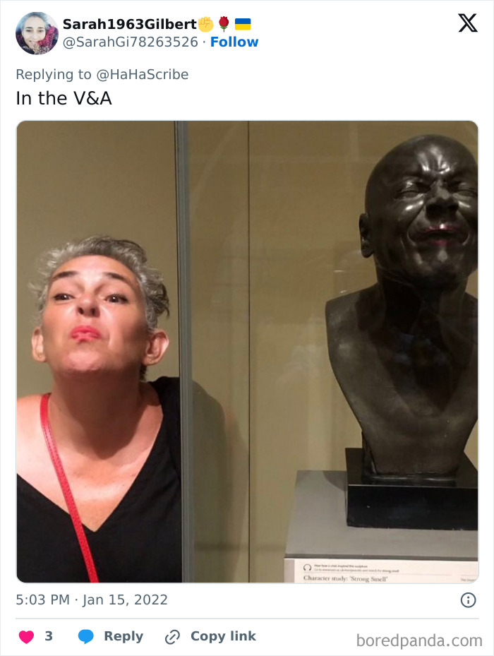 Woman mimics facial expression of sculpture in museum glass case, showcasing life imitating art moment.
