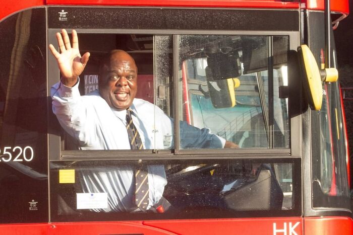 Friendly bus driver in uniform smiling and waving through the window, part of wholesome posts to distract from world horrors