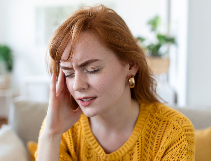 Young woman wearing a yellow sweater, holding her head in distress, representing betrayal and affair emotions at home.