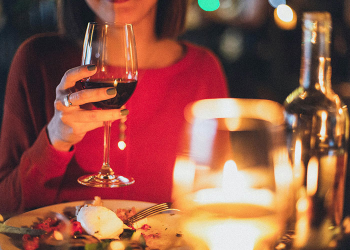 Woman in red sweater holding wine glass at candlelit dinner, illustrating creepy things women do that cross the line according to men.