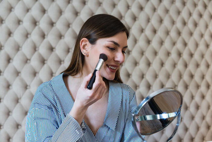 Woman applying makeup using a brush in front of a mirror, relating to women revealing absurd relationship dealbreakers.
