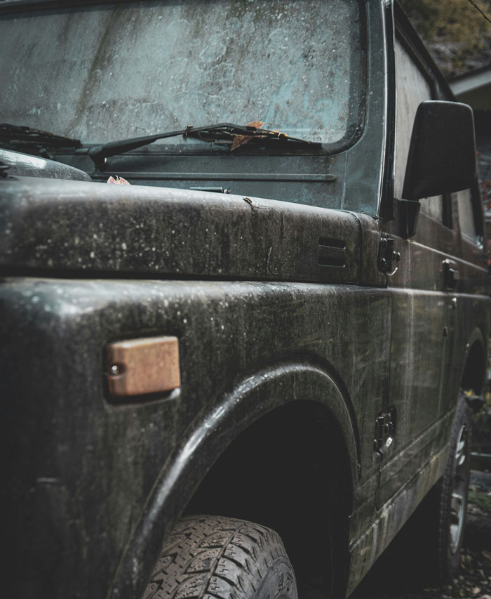 Old dirty police SUV parked outdoors, showing grime-covered windshield and rugged tire, evoking police horror stories.
