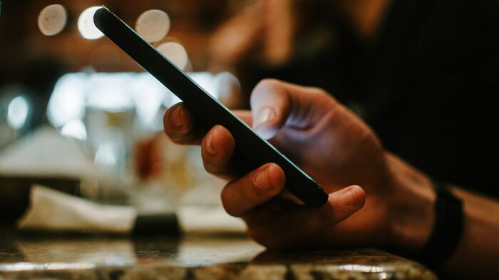 A food delivery driver holding a smartphone, checking chaotic stories shared on a dimly lit background.