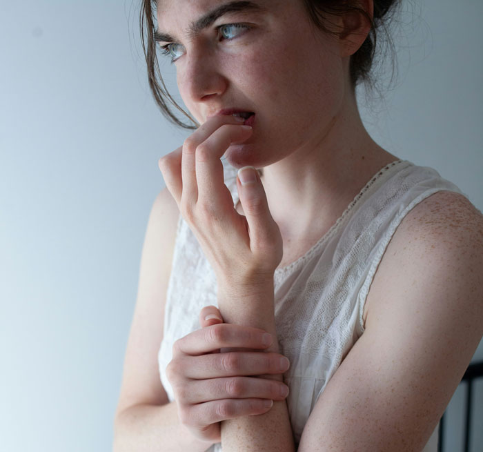 Young woman in a white sleeveless top, showing nervous behavior, illustrating unexpected things men didn’t know about women dating