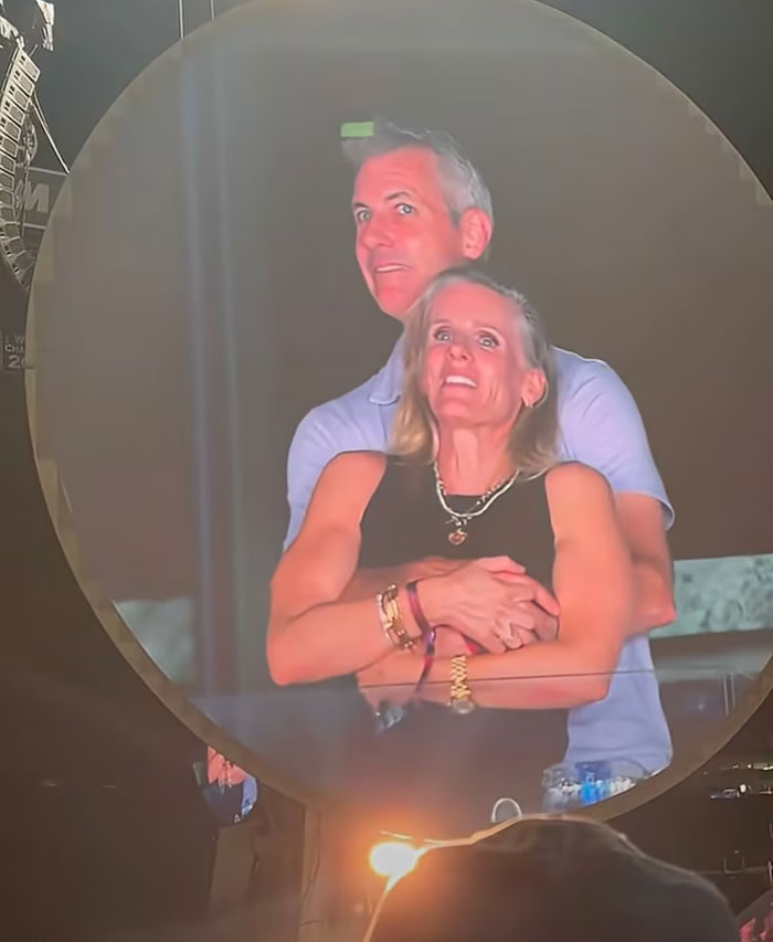 Middle-aged couple hugging and watching a concert, captured on a large round screen during a live event.
