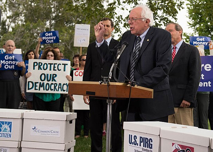 Bernie Sanders speaking at a rally about democracy and political reform amid concerns over historical events damage to society.