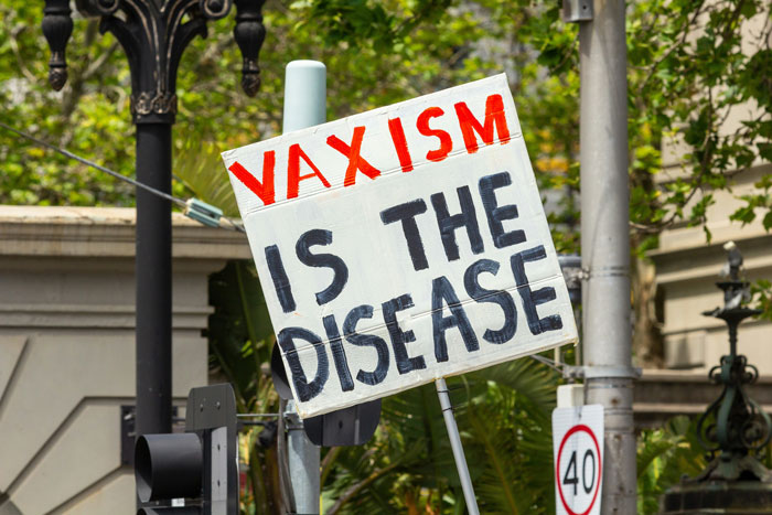 Protest sign reading Vaxism is the disease at a public demonstration, highlighting groups of stupid people behavior.