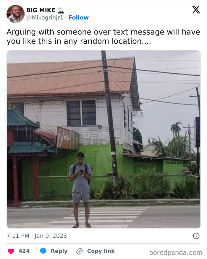 Man standing in the middle of a street crosswalk, focused on his phone, illustrating specific moments in our lives.