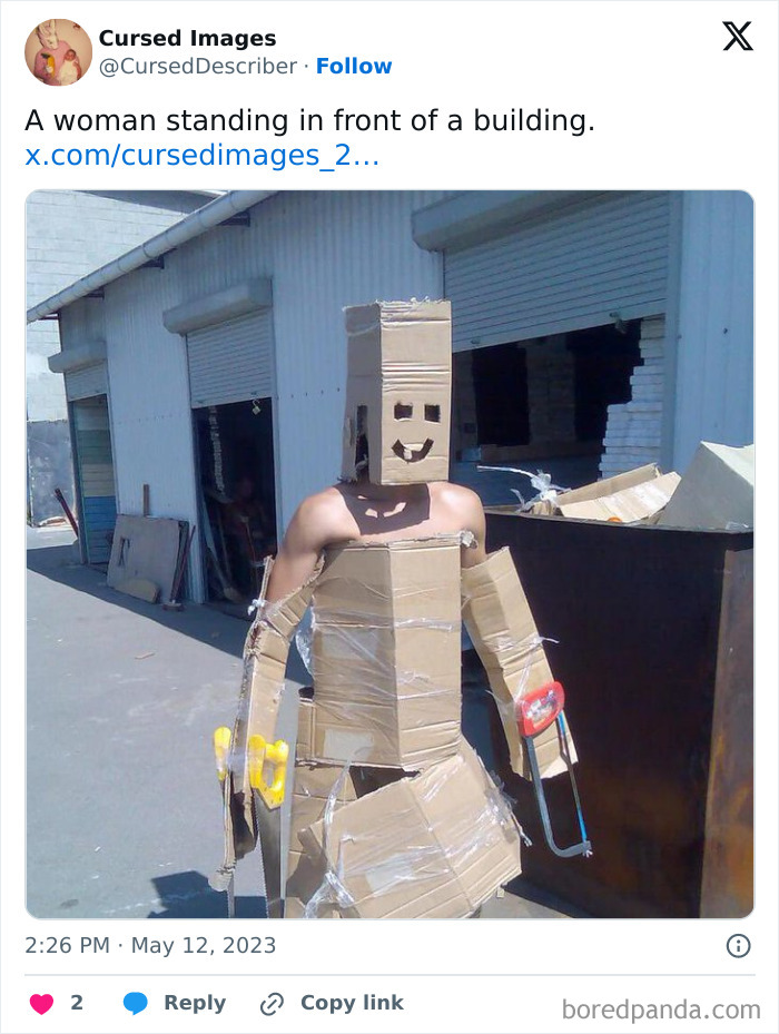 Person dressed in disturbing cardboard costume with a smiley face mask, holding crutches near a building outdoors.