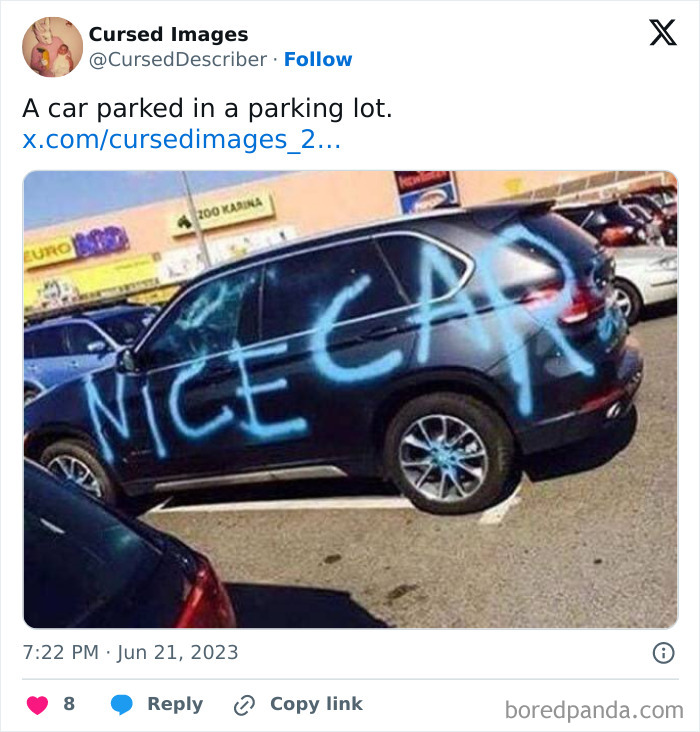 Black SUV spray-painted with large blue graffiti reading nice car, parked incorrectly across two spots in a parking lot.
