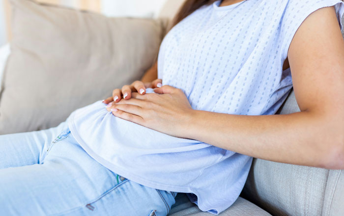 Woman resting on couch with hands on abdomen, illustrating unexpected things men didn’t know about women in dating.