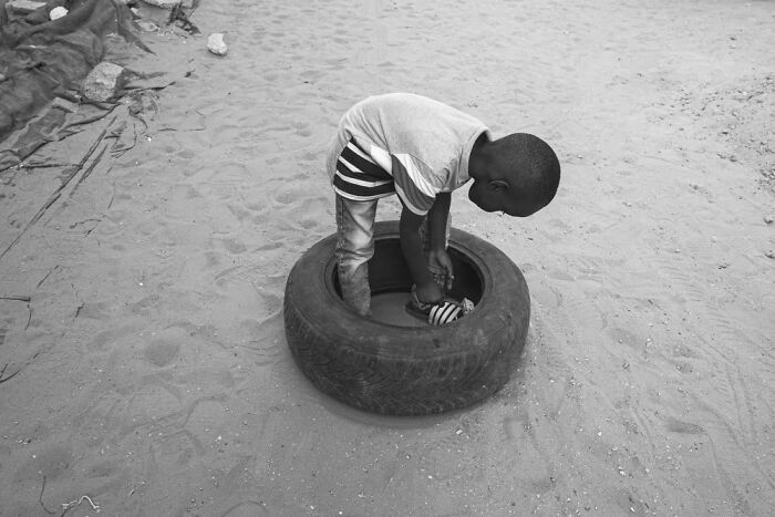 Child playing inside a tire on sandy ground, representing diverse children of the world in powerful photographs.