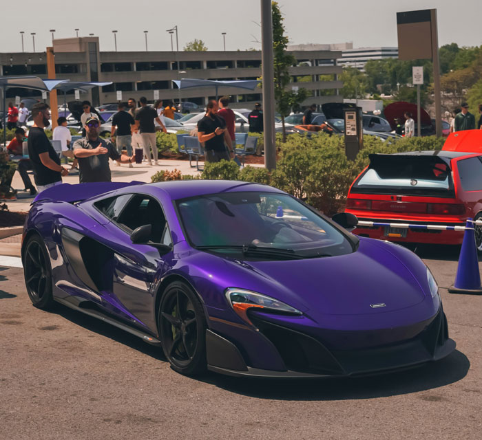 Purple luxury sports car parked outdoors at a crowded event, highlighting groups of stupid people in public settings.