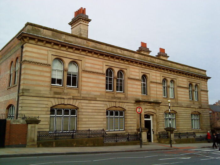Historic stone building on a city street with people walking, related to meningitis misdiagnosis involving a girl, 15 years old.