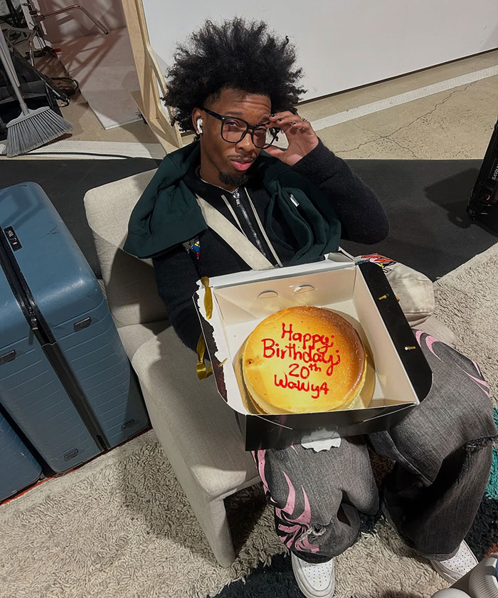 Young man holding birthday cake sitting on a chair near luggage, related to abandoned Tesla registered to singer news story
