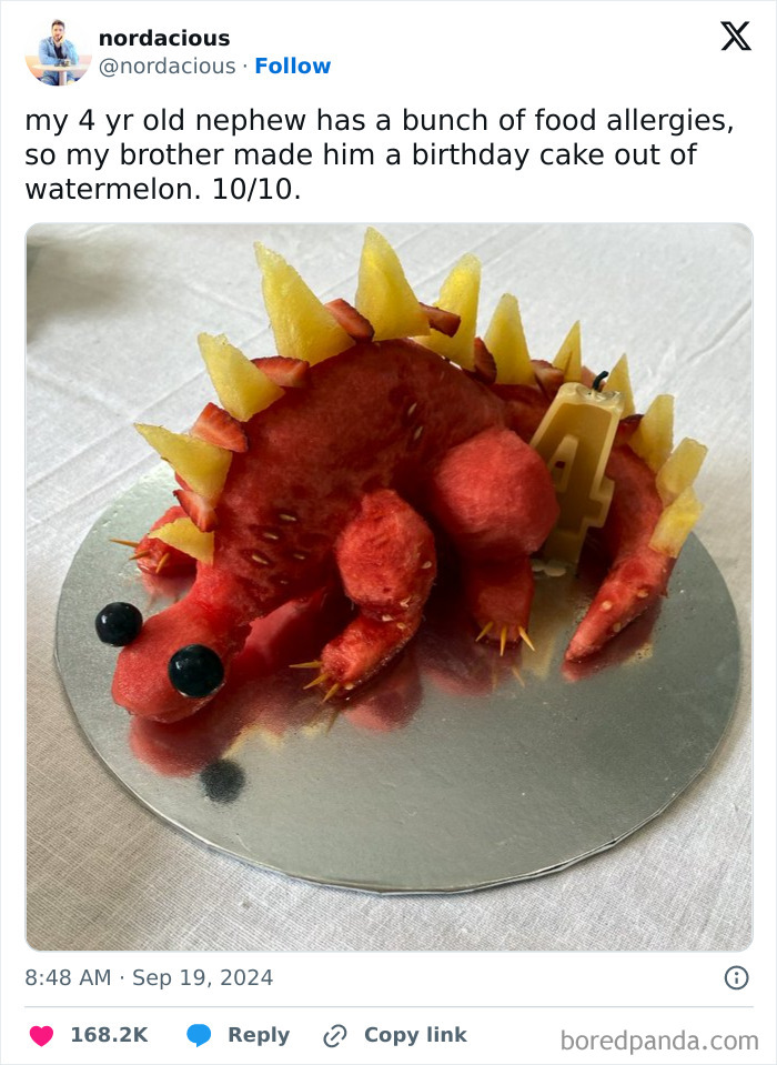 Creative birthday cake made of watermelon shaped like a dinosaur with fruit spikes, a wholesome post to distract from world horrors.
