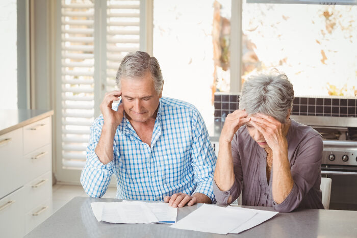 Older couple in kitchen stressed while reviewing shocking family secrets revealed in documents on table