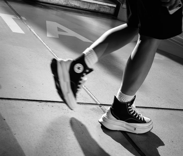 Black and white photo of person walking on pavement wearing high-top sneakers, illustrating clever loopholes exploited creatively.