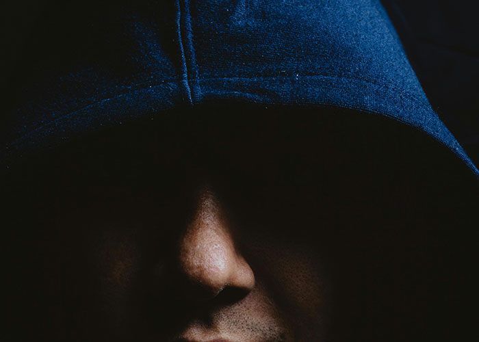 Close-up of a person wearing a dark hood in low light, evoking a sense of terrifying true stories and mystery.