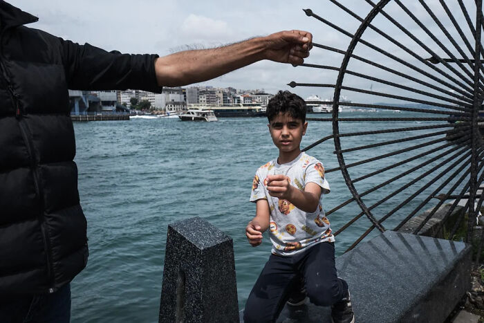 Young boy near waterfront, engaging with an adult, captured in powerful children of the world photograph.