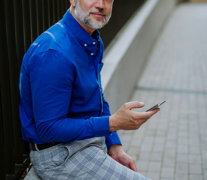 Hombre con camisa azul sentado, usando teléfono móvil para descubrir verdades ocultas en su entorno cotidiano.