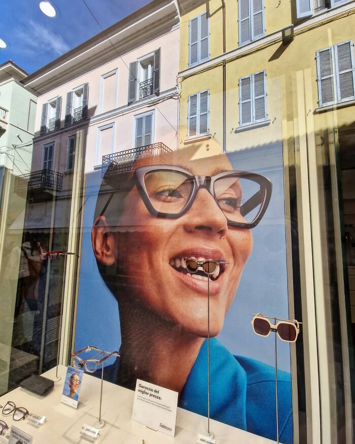 Street photo showing a reflection creating a funny coincidence with a sunglasses ad in a storefront window.