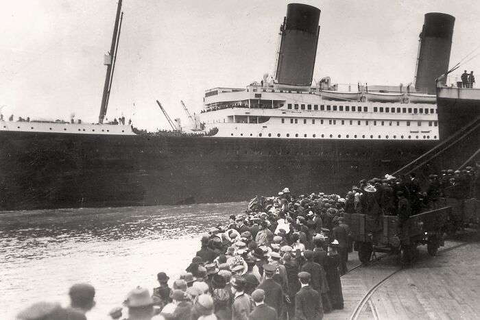 Crowd gathered at pier beside Titanic ship, showcasing rare historical moment before its famous voyage.