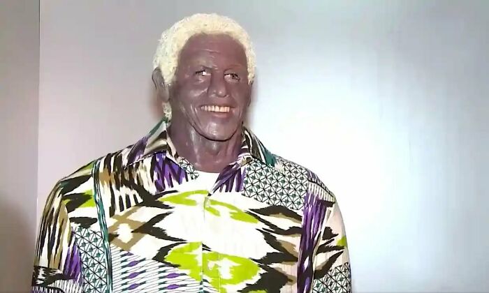 Wax sculpture of a famous figure with an unusual expression wearing a colorful patterned shirt, part of creepy wax sculptures.