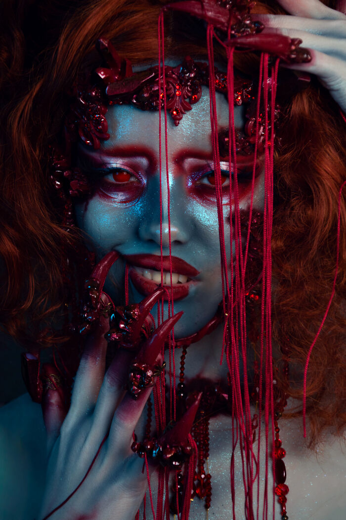 Person transformed into a haunting Halloween character with red makeup, elaborate claws, and red string details for spooky effect.