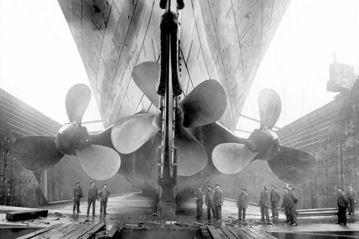 Rare historical photo of the Titanic’s propellers with workers standing in a dry dock during ship construction.