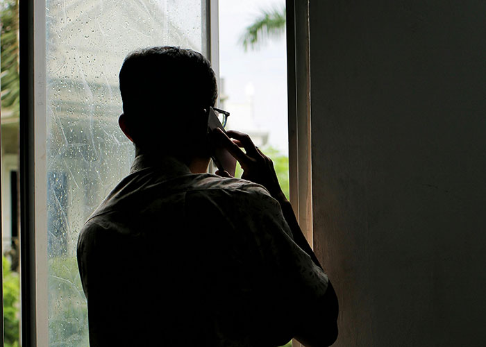 Silhouette of a man making a phone call inside near window, related to neighbor cutting down white oak trees without permission case.
