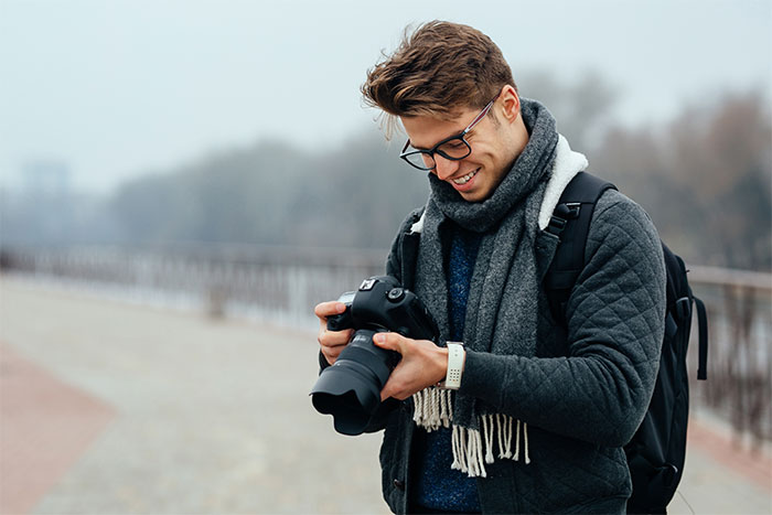 Young man holding a camera outdoors, smiling while reviewing photos, illustrating a story about catching a friend stealing.