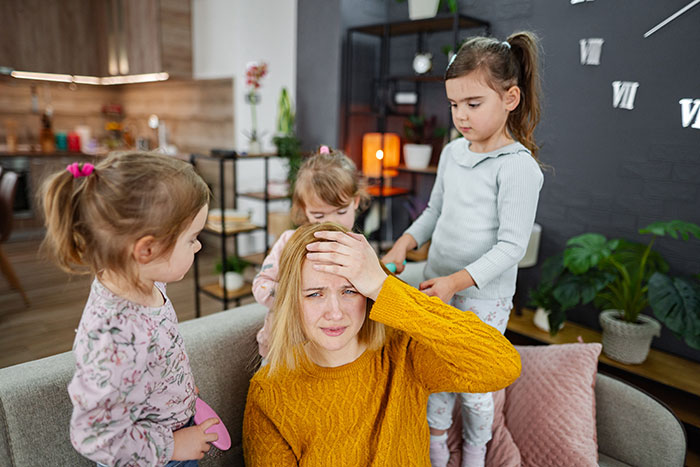 Woman in mustard sweater looking stressed while nannying children at home, suspecting husband's coworker involvement.