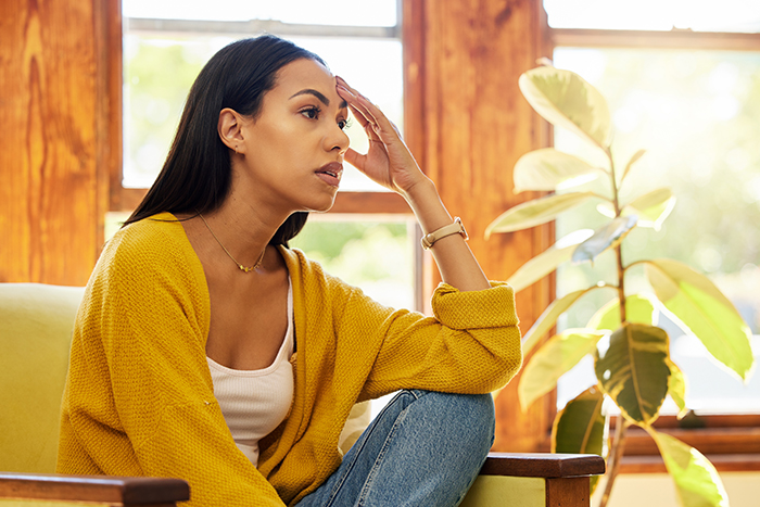 Woman in a yellow sweater sitting thoughtfully by a window, reflecting on renting out husband&rsquo;s man cave after his refusal to help.