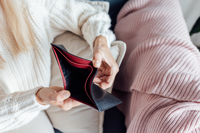 Person in a white sweater showing an empty black wallet, symbolizing no money for honeymoon tickets.