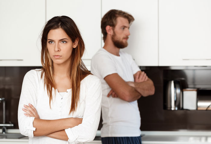 Man and wife in kitchen facing away from each other, man visibly upset showing he hates how easy things come to wife. Man and wife in kitchen facing away from each other, man visibly upset showing he hates how easy things come to wife.