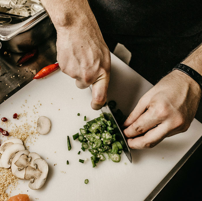 Hands chopping vegetables on a white cutting board preparing food that may trigger a teen allergic reaction at a friend’s house. Hands chopping vegetables on a white cutting board preparing food that may trigger a teen allergic reaction at a friend’s house.