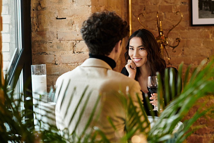 Woman and man on a date in a cozy restaurant, with the woman smiling and holding a glass of red wine.