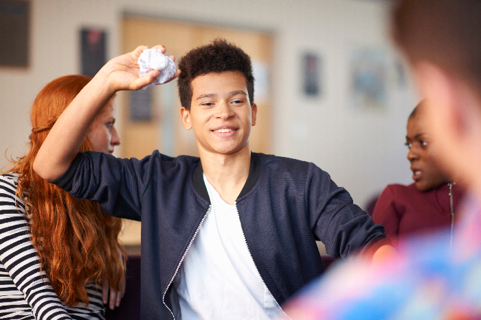 Young man confidently throwing a crumpled paper, symbolizing a man crushing former bully&rsquo;s ego at class reunion.