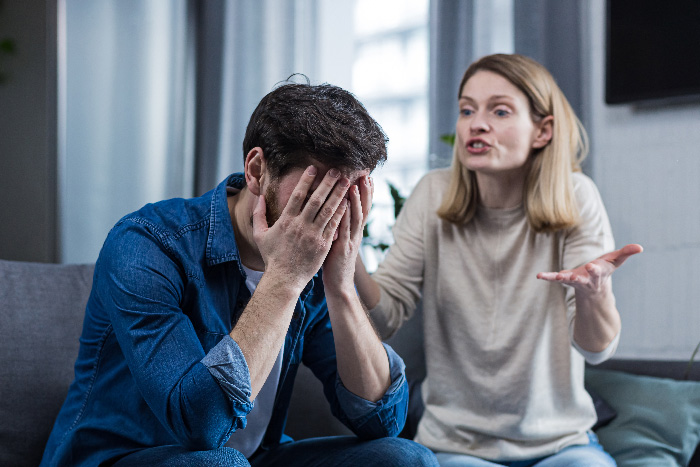 Man and woman having a heated argument on couch, illustrating a man jokes about trading wife for younger woman concept.