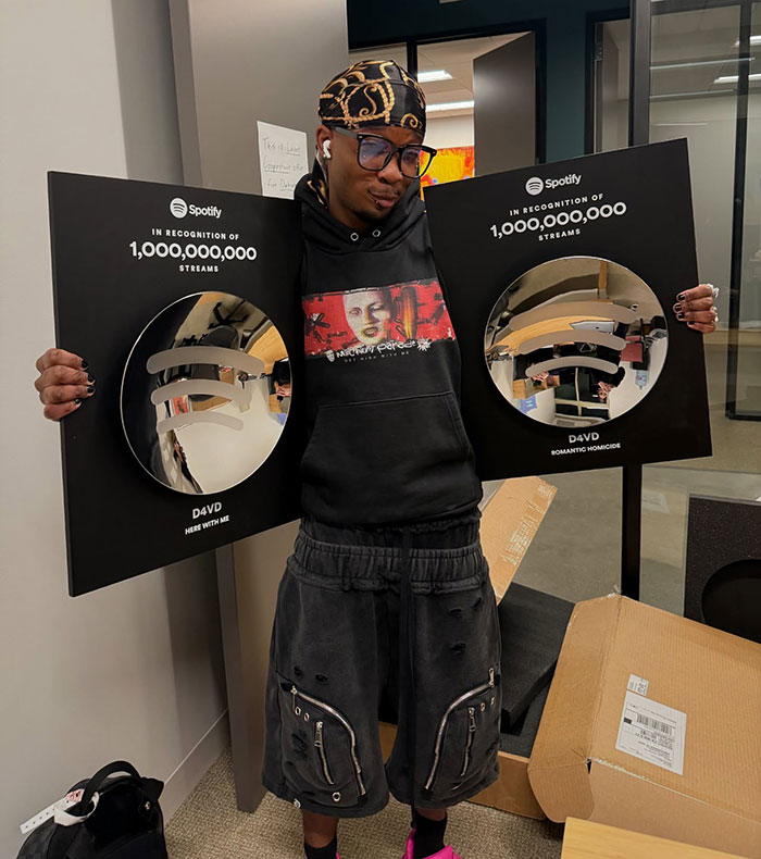Singer holding two Spotify plaques for 1 billion streams, relating to decomposing body found in abandoned Tesla case.