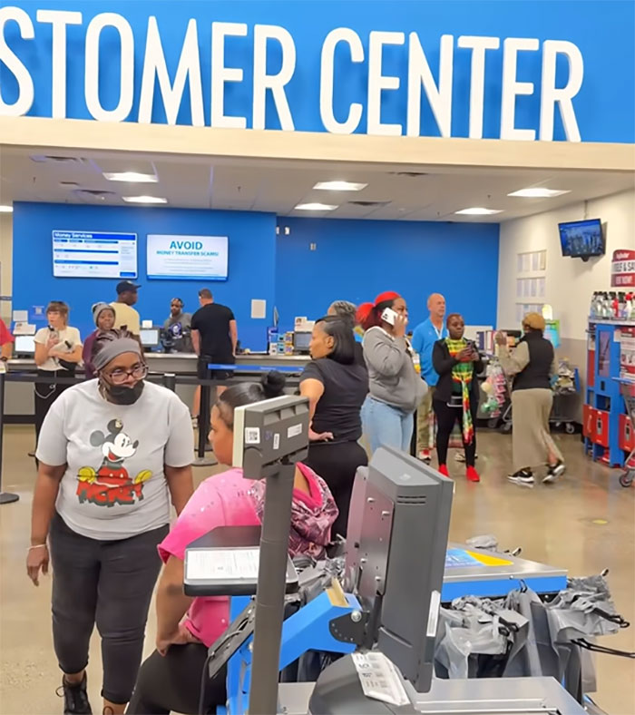 Walmart employee confronts an angry mob inside store customer center with multiple people gathered and interacting.