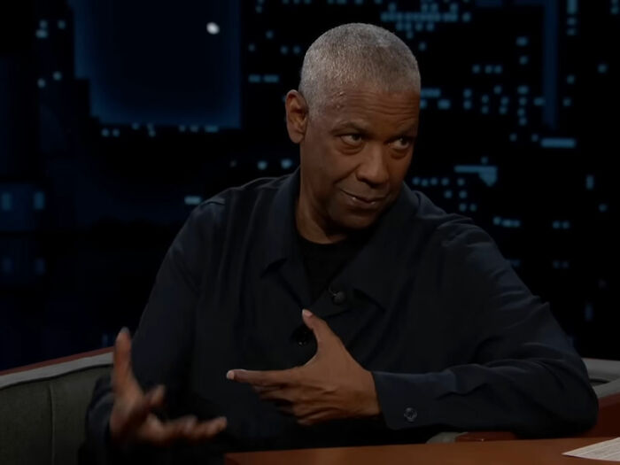 Denzel Washington in a dark shirt, seated during a talk show, explaining the correct way to pronounce his name. Denzel Washington in a dark shirt, seated during a talk show, explaining the correct way to pronounce his name.
