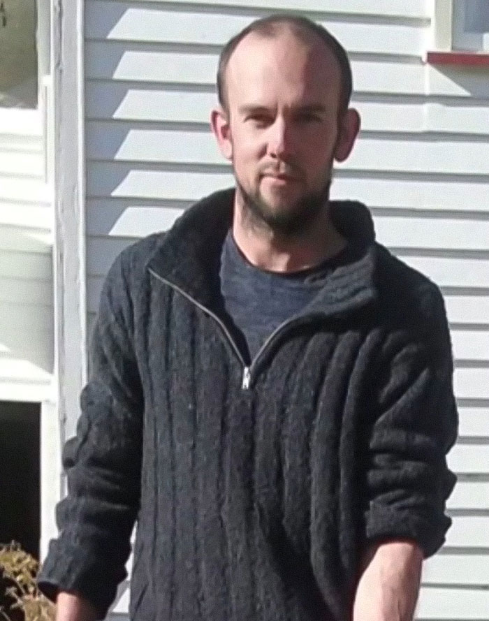 Man wearing a dark zip-up sweater standing outside a white house linked to fugitive dad in police standoff with kids