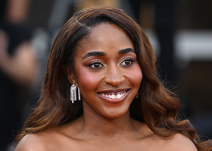 Actress Ayo Edebiri smiling at an event, wearing elegant earrings and styled hair in a bright setting.