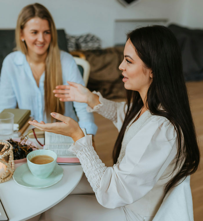 Two women having a conversation over coffee in a cozy setting, discussing sleep as a life-changing cheat code.