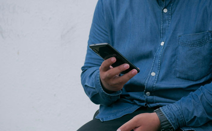 Person in blue shirt holding a smartphone, illustrating creepy things that happened while being home alone.