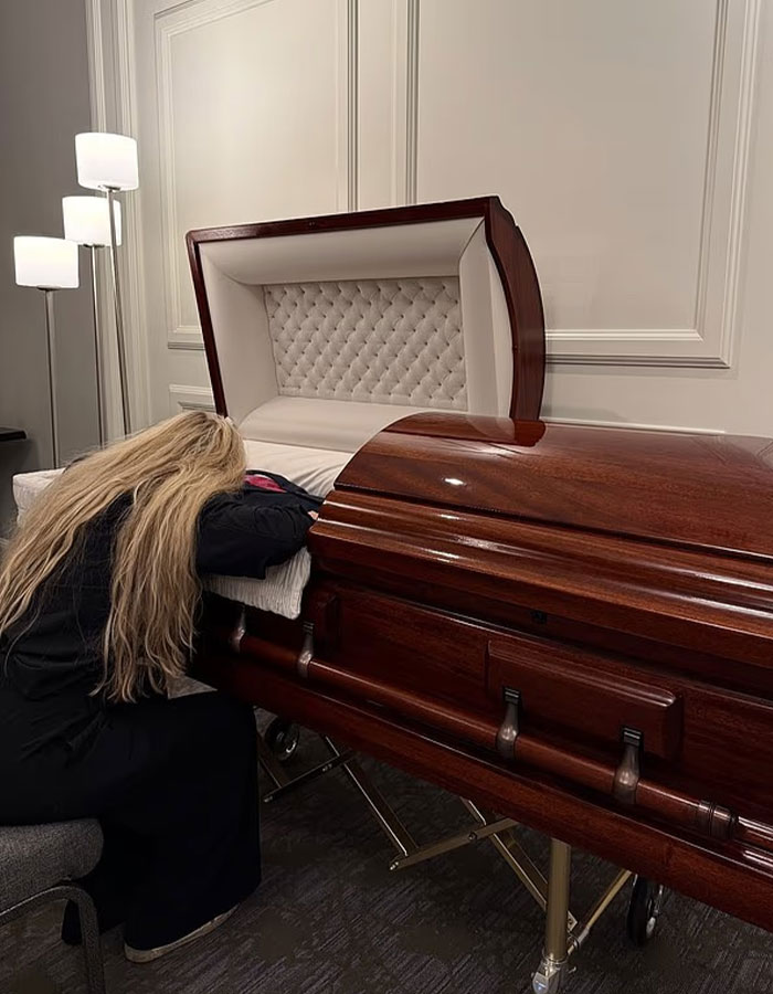 Woman with long blonde hair leaning on a wooden casket, expressing grief during a farewell gathering for justice seekers.