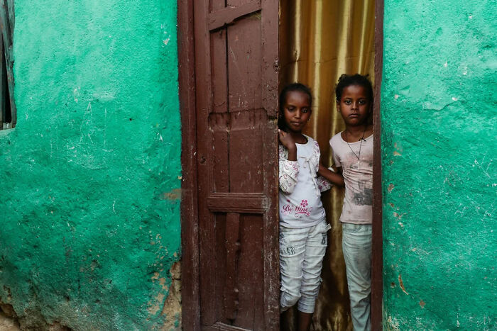 Two children standing in a doorway framed by a weathered green wall, captured in powerful photographs of children.