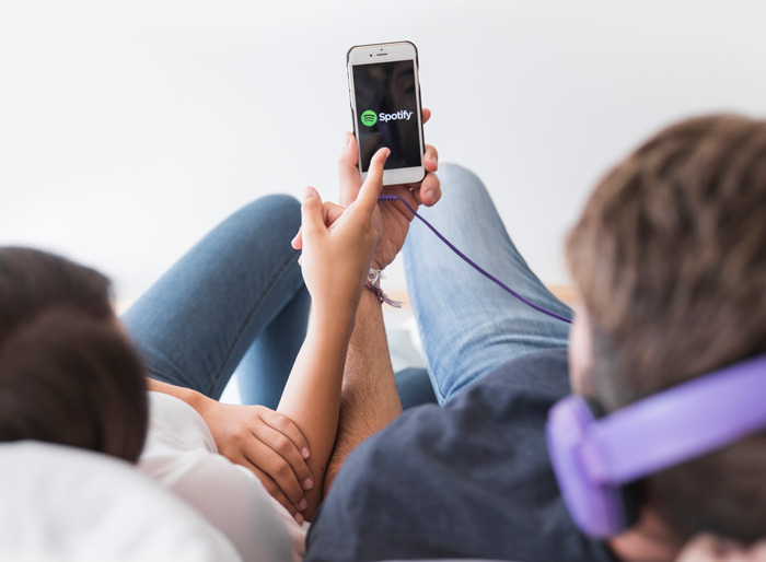 Two people lying down, looking at a phone screen with Spotify, a glance at a phone changing everything moment.